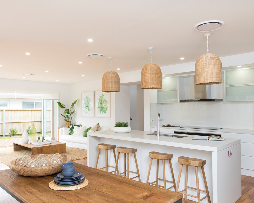 Design ideas for a medium sized coastal open plan kitchen in Wollongong with a double-bowl sink, glass-front cabinets, white splashback, stainless steel appliances, medium hardwood flooring, an island and white worktops.