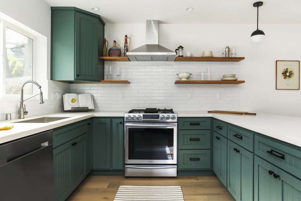 Traditional u-shaped kitchen in Los Angeles with a submerged sink, recessed-panel cabinets, green cabinets, white splashback, metro tiled splashback, stainless steel appliances, light hardwood flooring, a breakfast bar and white worktops.