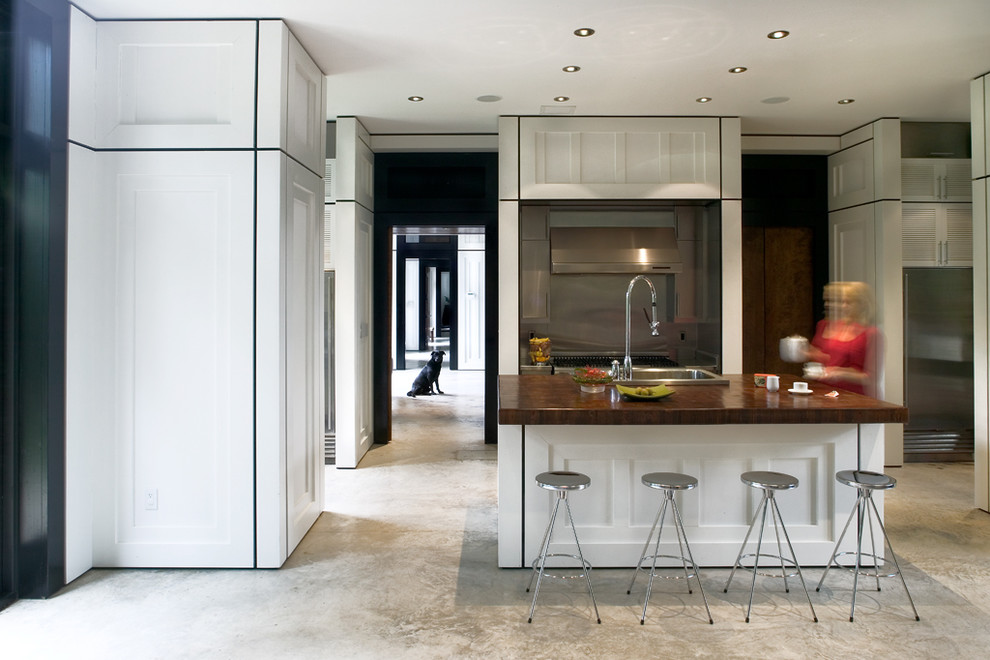 Bild på ett stort funkis kök, med rostfria vitvaror, en nedsänkt diskho, luckor med infälld panel, vita skåp, granitbänkskiva, grått stänkskydd, stänkskydd i metallkakel, betonggolv, en köksö och grått golv