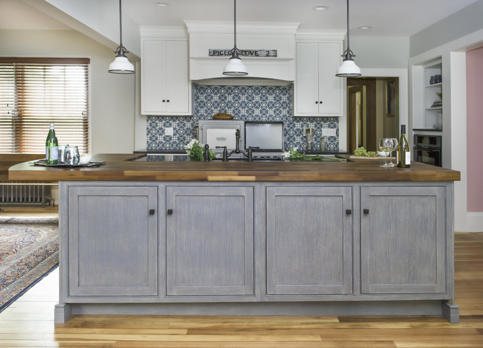 Mid-sized mountain style galley medium tone wood floor and brown floor open concept kitchen photo in Boston with a farmhouse sink, beaded inset cabinets, white cabinets, wood countertops, blue backsplash, cement tile backsplash, paneled appliances, an island and black countertops