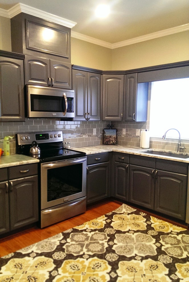 Mid-sized trendy l-shaped medium tone wood floor enclosed kitchen photo in Atlanta with an undermount sink, raised-panel cabinets, gray cabinets, marble countertops, gray backsplash, subway tile backsplash, stainless steel appliances and an island