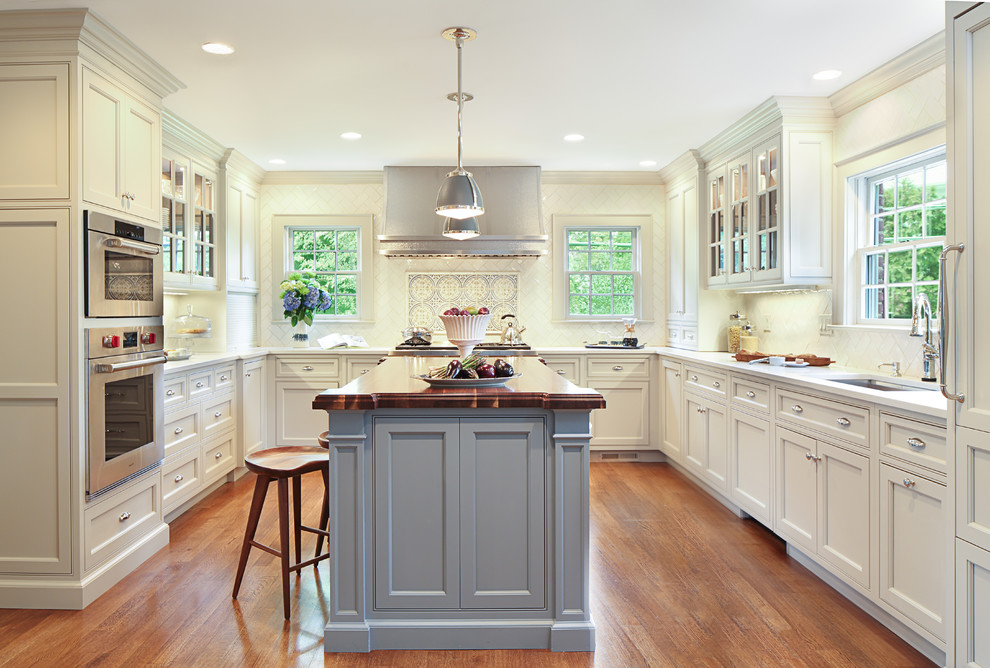 Immagine di una cucina classica con lavello sottopiano, ante a filo, ante bianche, paraspruzzi bianco, elettrodomestici in acciaio inossidabile, pavimento in legno massello medio e pavimento marrone
