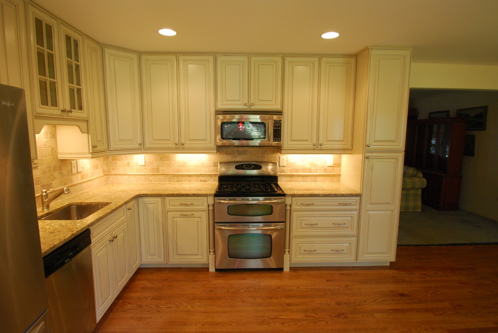 Eat-in kitchen - mid-sized traditional l-shaped light wood floor eat-in kitchen idea in DC Metro with an undermount sink, raised-panel cabinets, white cabinets, granite countertops, beige backsplash, porcelain backsplash, stainless steel appliances and no island