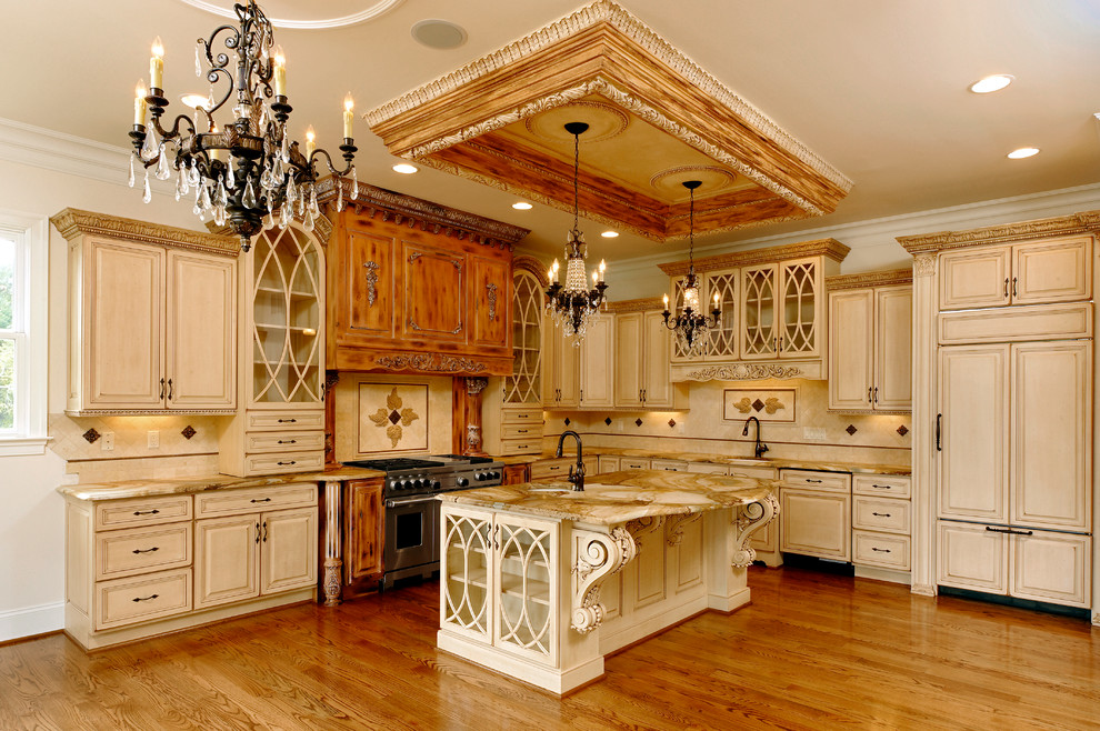 Example of a large tuscan l-shaped medium tone wood floor and brown floor kitchen design in DC Metro with an undermount sink, raised-panel cabinets, beige cabinets, marble countertops, beige backsplash, stone tile backsplash, paneled appliances and an island