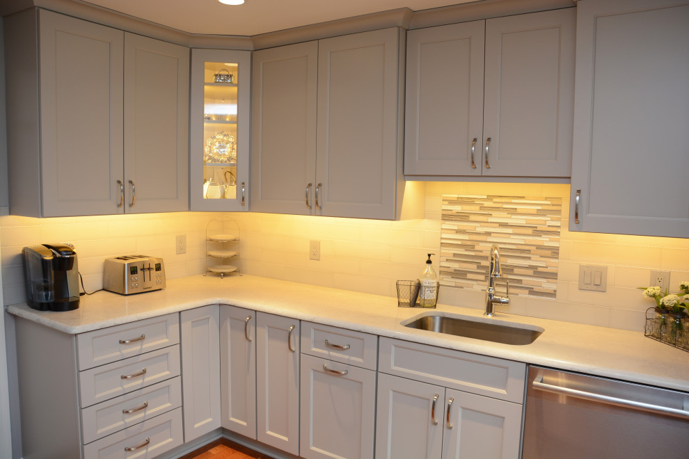 Bild på ett avskilt, mellanstort vintage vit vitt u-kök, med en undermonterad diskho, luckor med infälld panel, grå skåp, bänkskiva i kvarts, vitt stänkskydd, rostfria vitvaror, mellanmörkt trägolv, en halv köksö och brunt golv