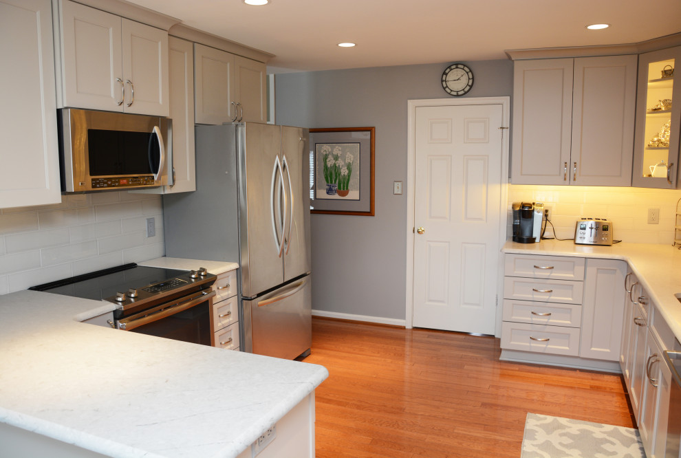 Exempel på ett avskilt, mellanstort klassiskt vit vitt u-kök, med en undermonterad diskho, luckor med infälld panel, grå skåp, bänkskiva i kvarts, vitt stänkskydd, rostfria vitvaror, mellanmörkt trägolv, en halv köksö och brunt golv