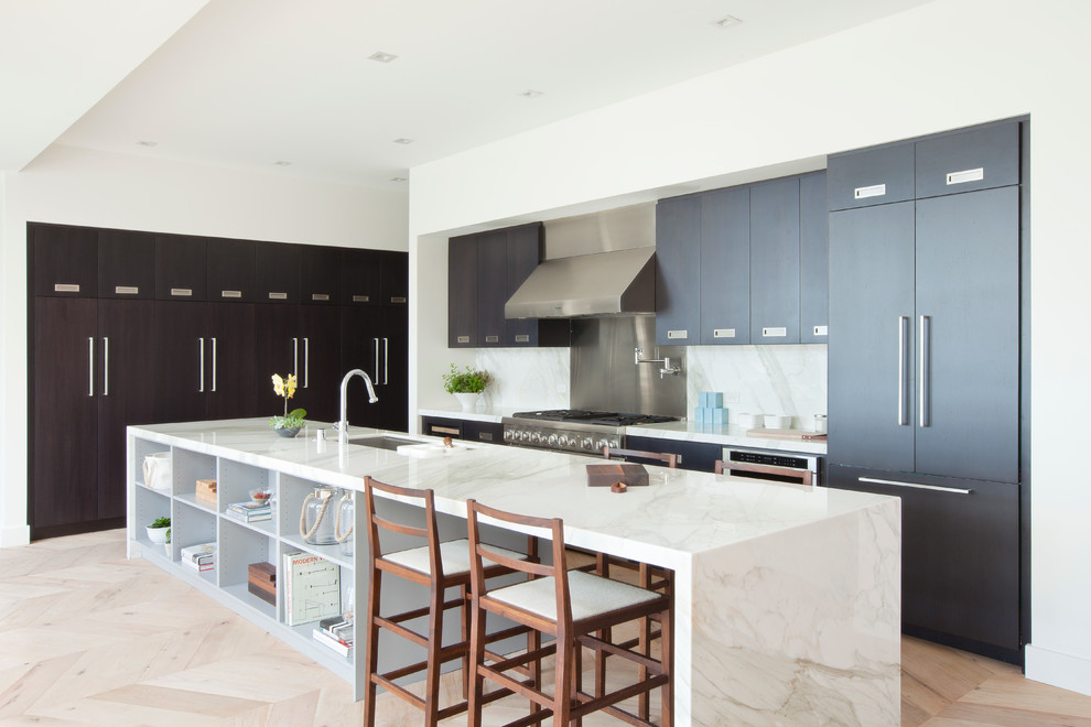 Medium sized contemporary single-wall open plan kitchen in Los Angeles with a submerged sink, flat-panel cabinets, dark wood cabinets, marble worktops, white splashback, stone slab splashback, light hardwood flooring, an island and integrated appliances.