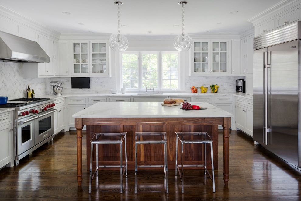 This is an example of a traditional u-shaped kitchen in Boston with shaker cabinets, white cabinets, white splashback, stainless steel appliances, dark hardwood flooring and an island.