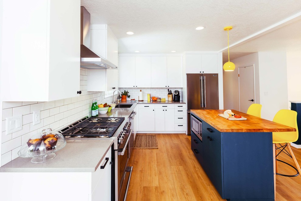Example of a mid-sized trendy l-shaped vinyl floor and brown floor eat-in kitchen design in Portland with an undermount sink, flat-panel cabinets, white cabinets, quartz countertops, white backsplash, subway tile backsplash, stainless steel appliances and an island