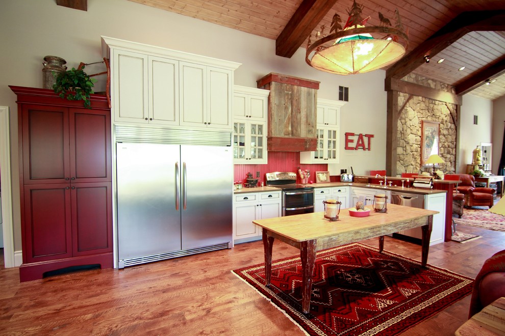 オースティンにあるカントリー風のおしゃれなアイランドキッチン (アンダーカウンターシンク、落し込みパネル扉のキャビネット、ヴィンテージ仕上げキャビネット、赤いキッチンパネル、シルバーの調理設備、無垢フローリング) の写真