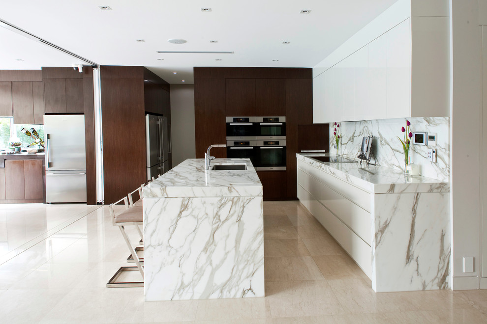 Foto di un cucina con isola centrale design con lavello sottopiano, ante lisce, ante bianche, paraspruzzi bianco e elettrodomestici in acciaio inossidabile