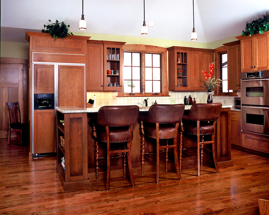 Aménagement d'une cuisine américaine craftsman en L et bois brun avec un placard à porte shaker, un électroménager en acier inoxydable, un sol en bois brun et îlot.