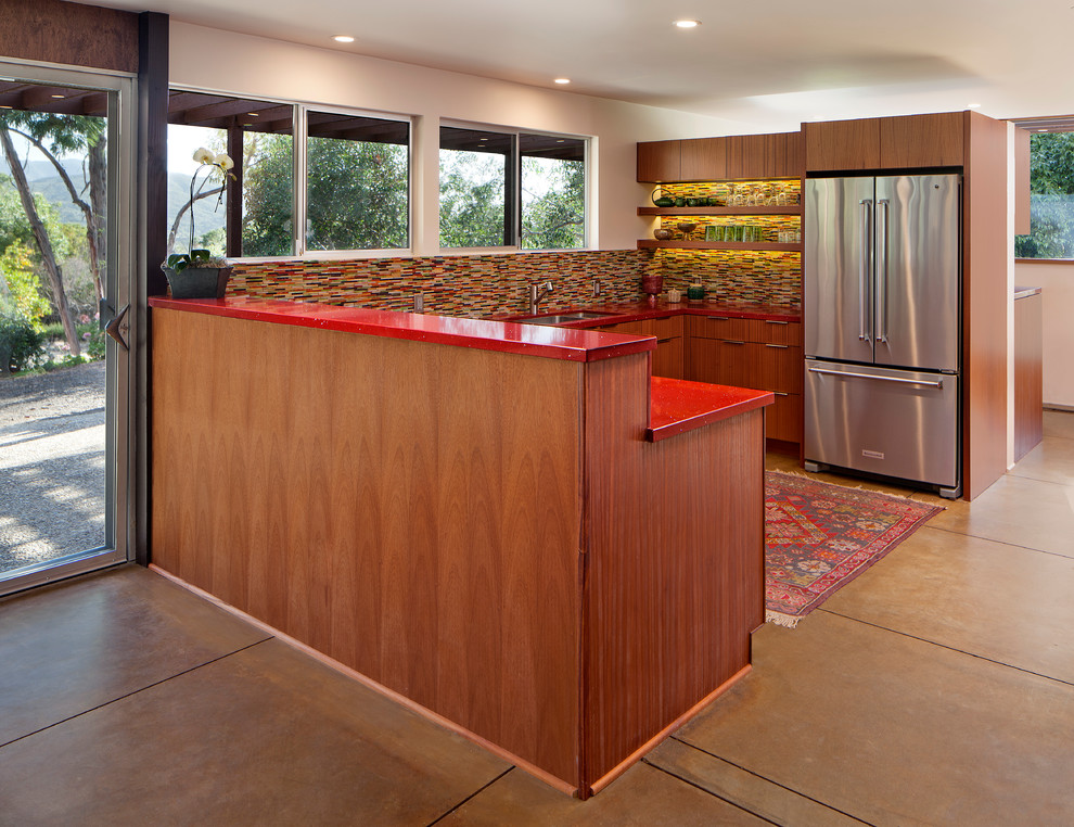 Design ideas for a medium sized midcentury u-shaped kitchen/diner in Los Angeles with a submerged sink, flat-panel cabinets, medium wood cabinets, engineered stone countertops, multi-coloured splashback, glass tiled splashback, stainless steel appliances, concrete flooring and a breakfast bar.