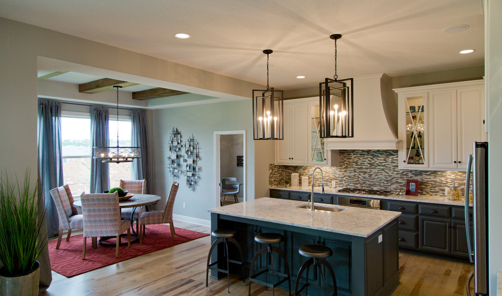Mid-sized transitional l-shaped light wood floor and brown floor open concept kitchen photo in Kansas City with an undermount sink, glass-front cabinets, white cabinets, granite countertops, multicolored backsplash, matchstick tile backsplash, stainless steel appliances and an island