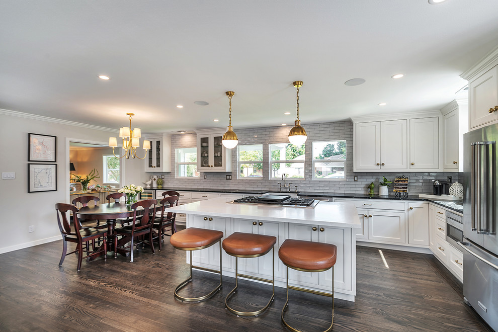 Large classic open plan kitchen in San Francisco with a belfast sink, beaded cabinets, white cabinets, engineered stone countertops, white splashback, metro tiled splashback, stainless steel appliances, medium hardwood flooring, an island, brown floors and white worktops.