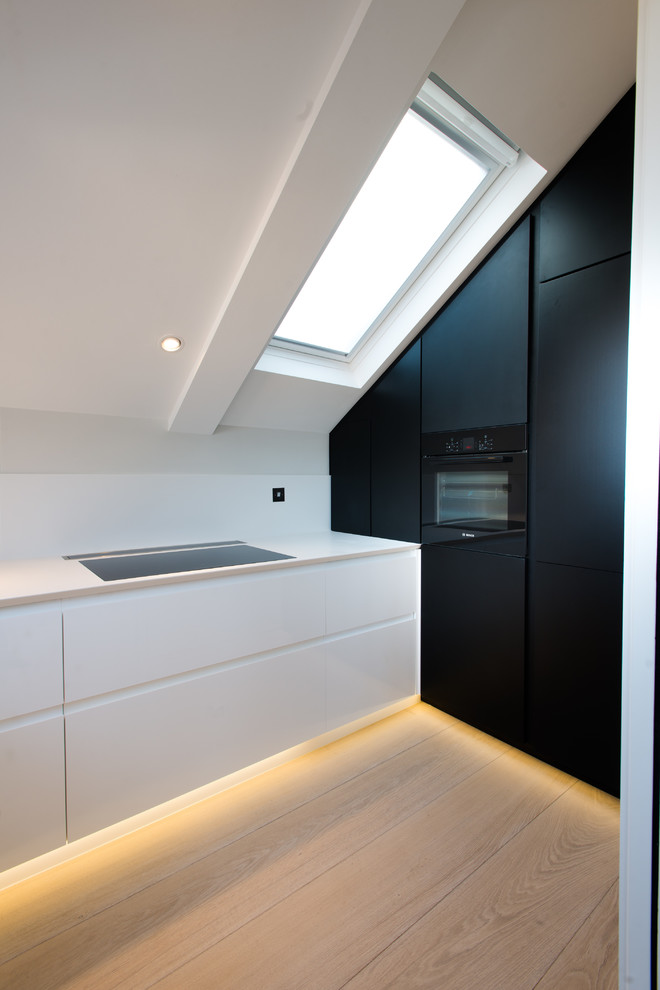 Moderne Küche ohne Insel mit Unterbauwaschbecken, flächenbündigen Schrankfronten, schwarzen Schränken, Küchenrückwand in Weiß, schwarzen Elektrogeräten und hellem Holzboden in London