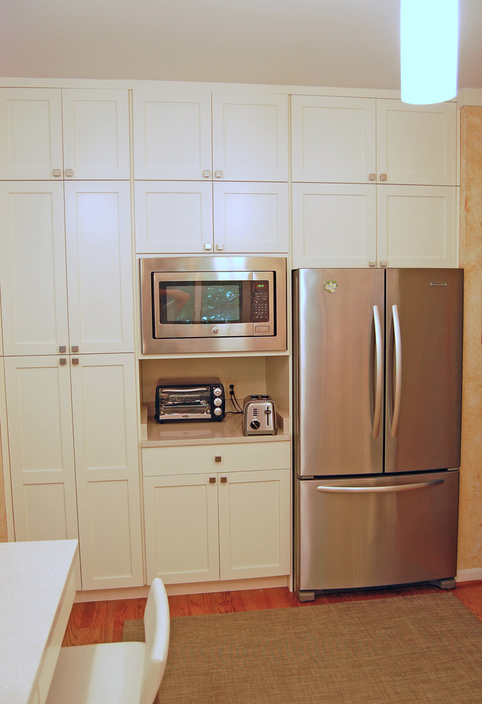 Amerikansk inredning av ett mellanstort kök, med en undermonterad diskho, skåp i shakerstil, vita skåp, bänkskiva i kvartsit, stänkskydd i porslinskakel, rostfria vitvaror, mellanmörkt trägolv och en halv köksö