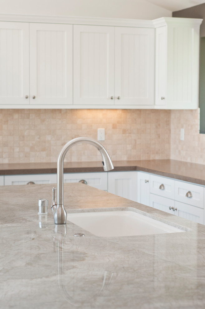 Large contemporary u-shaped open plan kitchen in Los Angeles with a submerged sink, beaded cabinets, white cabinets, granite worktops, beige splashback, travertine splashback, stainless steel appliances, dark hardwood flooring, an island, brown floors and beige worktops.