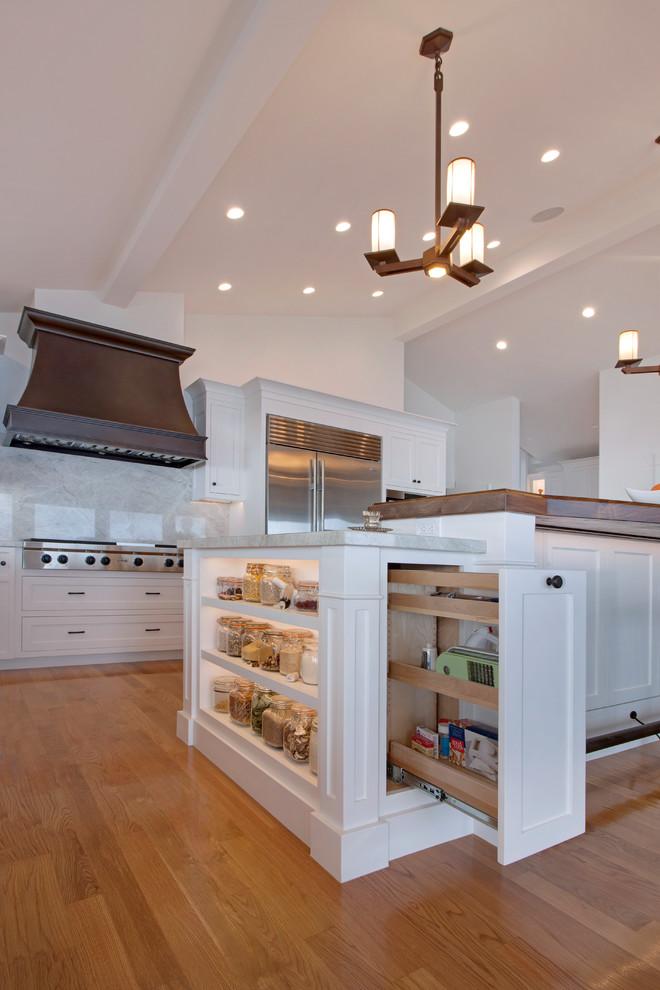 Klassisk inredning av ett mellanstort l-kök, med en undermonterad diskho, skåp i shakerstil, vita skåp, bänkskiva i kvartsit, vitt stänkskydd, stänkskydd i sten, rostfria vitvaror, ljust trägolv, en köksö och beiget golv