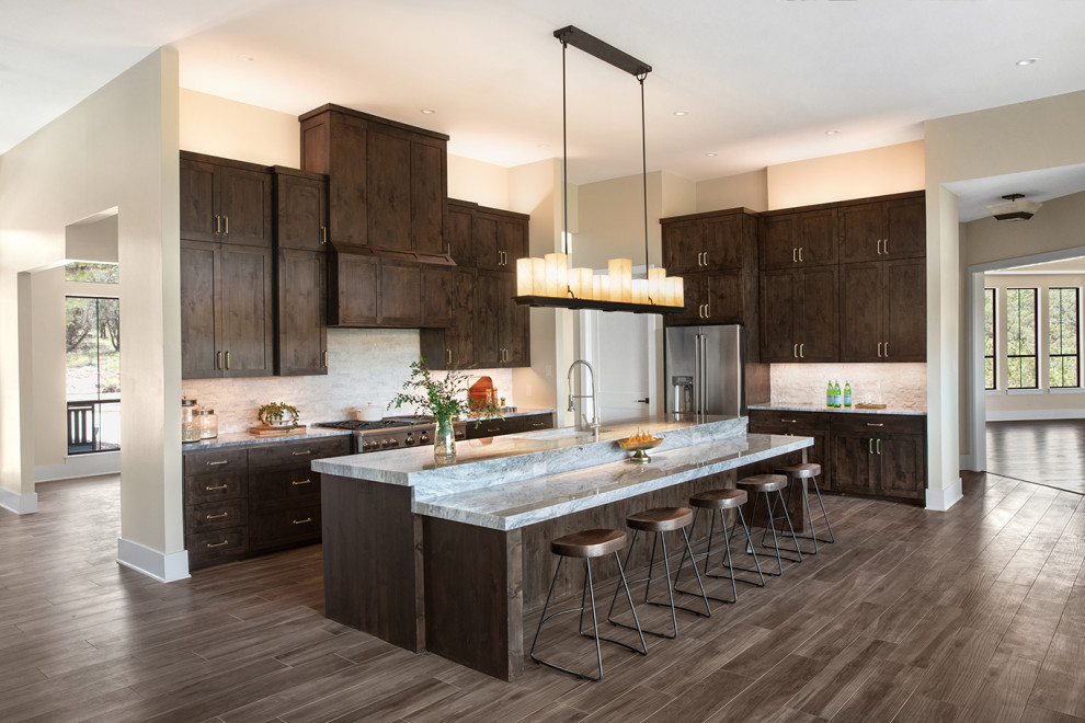 Example of a large transitional l-shaped dark wood floor and brown floor open concept kitchen design in Austin with an undermount sink, shaker cabinets, dark wood cabinets, quartzite countertops, gray backsplash, stone tile backsplash, stainless steel appliances, an island and gray countertops