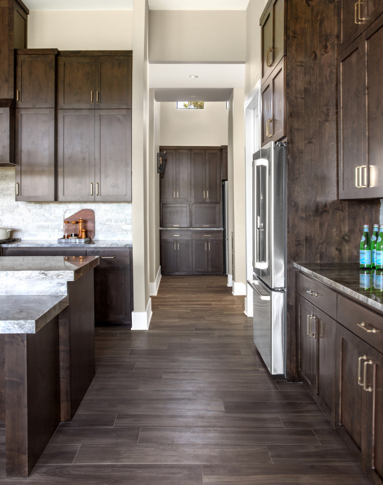 Large elegant galley porcelain tile and brown floor kitchen photo in Austin with an undermount sink, shaker cabinets, dark wood cabinets, granite countertops, gray backsplash, stone tile backsplash, stainless steel appliances, an island and gray countertops