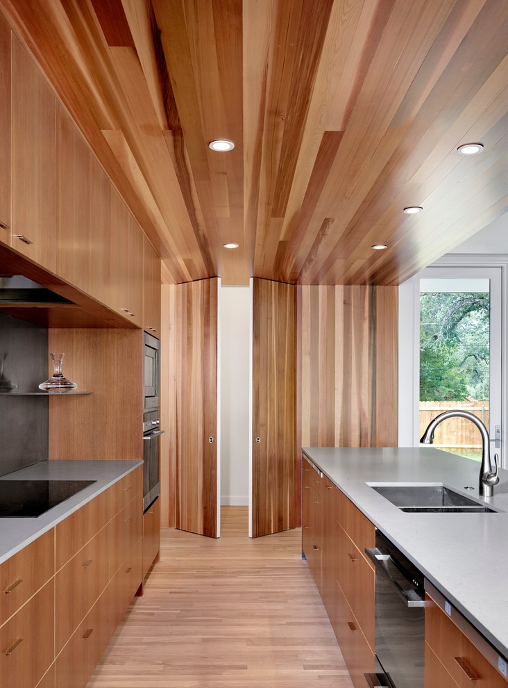 Idee per un cucina con isola centrale minimalista con ante lisce, ante in legno chiaro, elettrodomestici in acciaio inossidabile e parquet chiaro