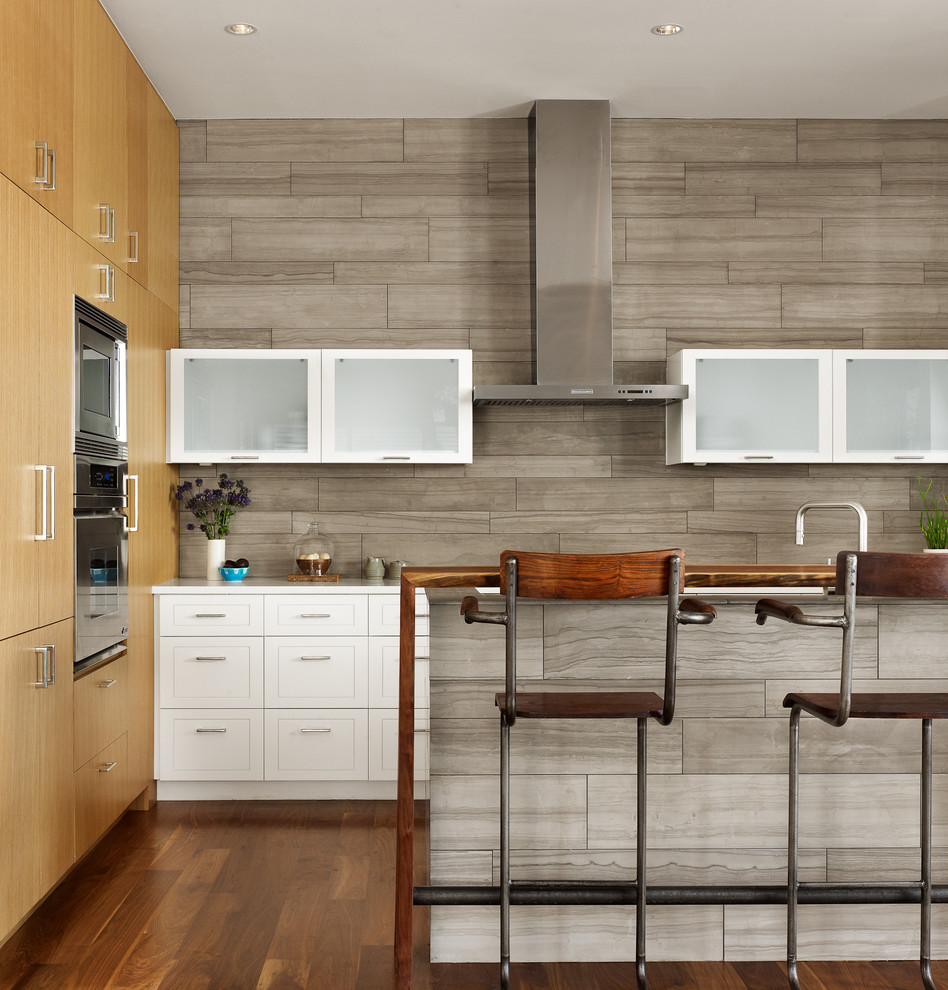This is an example of a contemporary galley kitchen in Austin with flat-panel cabinets, white cabinets, grey splashback and stainless steel appliances.