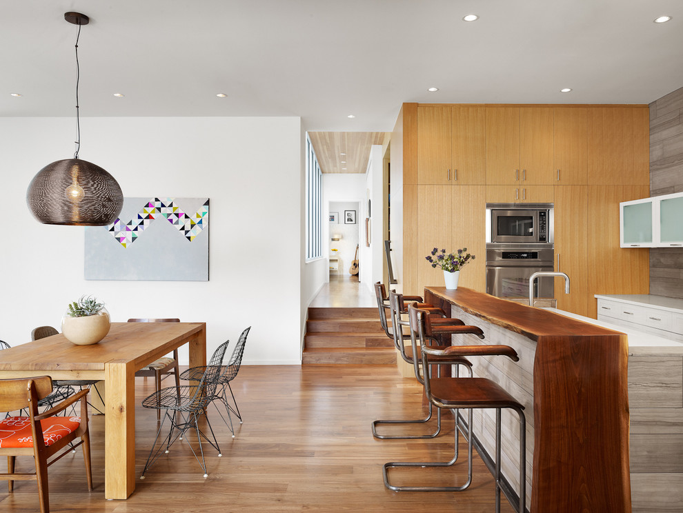 Cette photo montre une cuisine américaine parallèle tendance en bois clair avec un placard à porte plane, un plan de travail en bois et un électroménager en acier inoxydable.