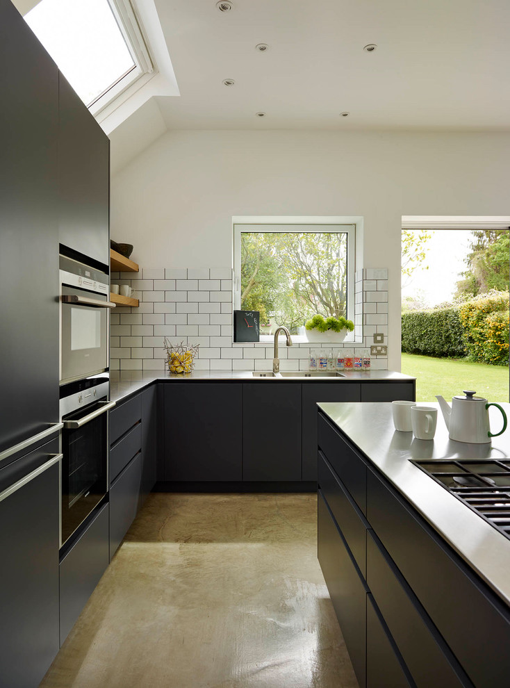 Idéer för ett stort modernt kök, med en integrerad diskho, släta luckor, svarta skåp, bänkskiva i rostfritt stål, vitt stänkskydd, stänkskydd i keramik, betonggolv och beiget golv