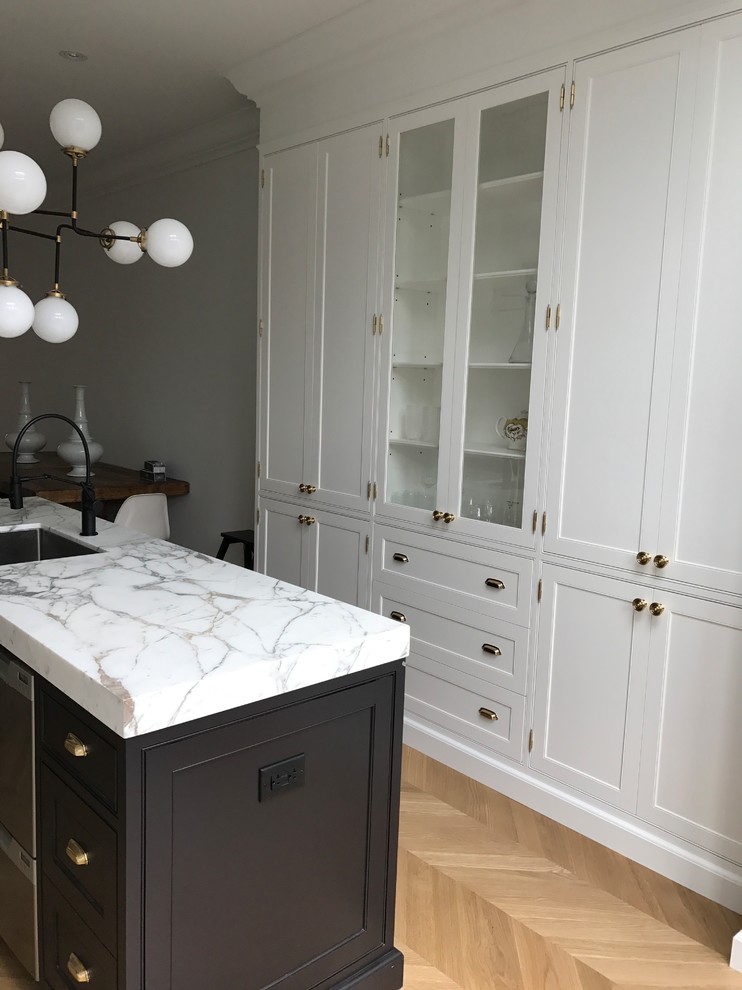 This is an example of a victorian galley kitchen pantry in Toronto with a submerged sink, recessed-panel cabinets, white cabinets, marble worktops, white splashback, porcelain splashback, stainless steel appliances, light hardwood flooring, an island and white worktops.