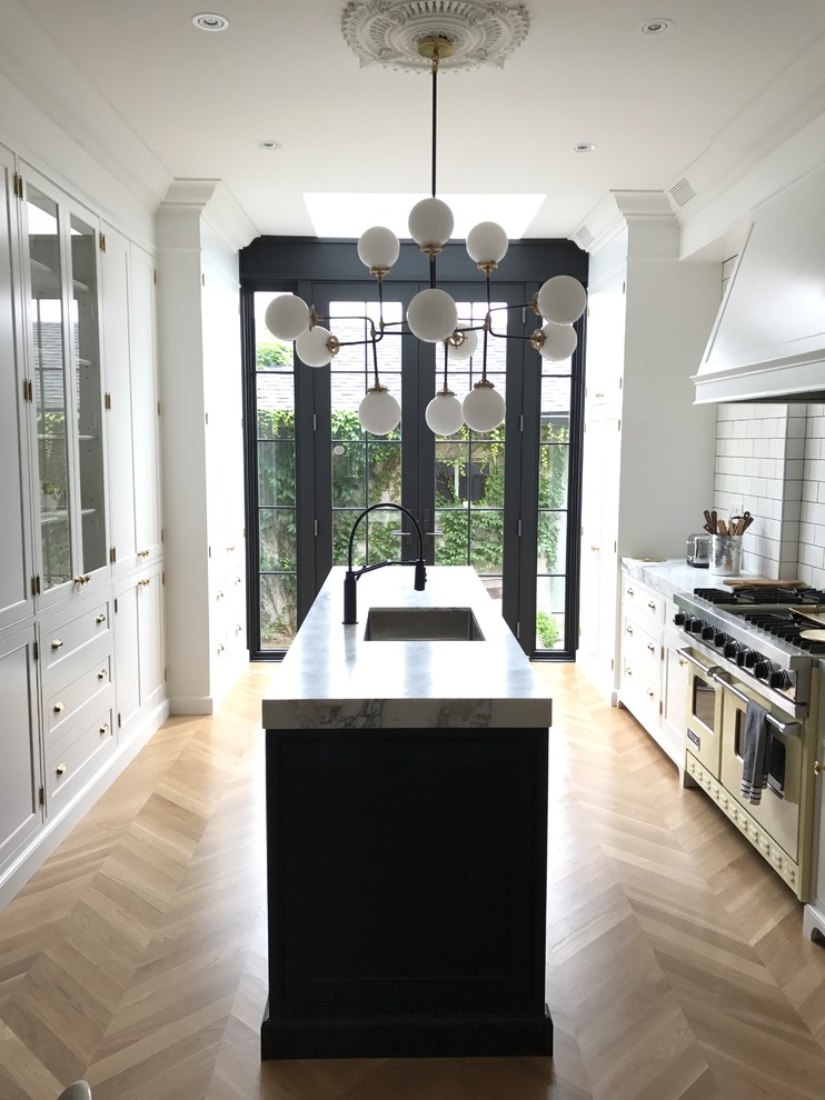 Kitchen pantry - victorian galley light wood floor kitchen pantry idea in Toronto with an undermount sink, recessed-panel cabinets, white cabinets, marble countertops, white backsplash, porcelain backsplash, stainless steel appliances, an island and white countertops
