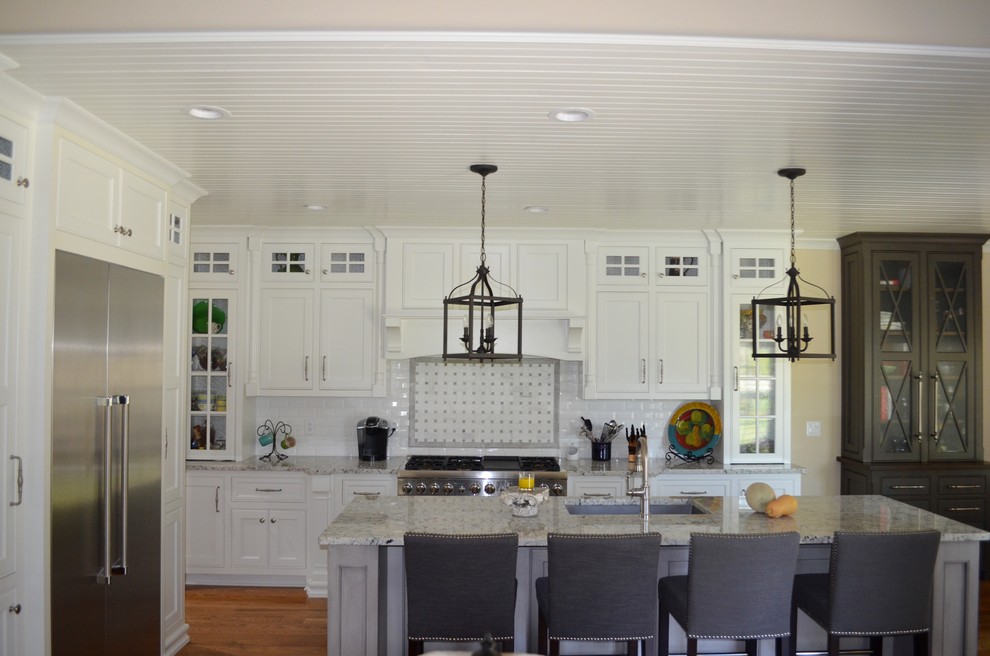 Klassisk inredning av ett mellanstort kök, med en enkel diskho, släta luckor, vita skåp, granitbänkskiva, vitt stänkskydd, stänkskydd i porslinskakel, rostfria vitvaror, mellanmörkt trägolv, en köksö och brunt golv