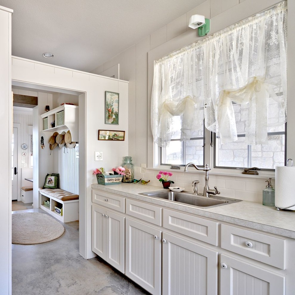 Shabby-Style Küche mit Einbauwaschbecken, weißen Schränken, Laminat-Arbeitsplatte, Küchenrückwand in Weiß, Rückwand aus Metrofliesen und Betonboden in Austin