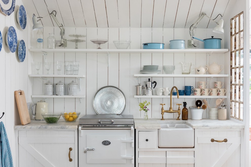 Shabby chic-inspirerad inredning av ett litet vit linjärt vitt kök, med en rustik diskho, vita skåp, marmorbänkskiva, vita vitvaror, öppna hyllor, vitt stänkskydd och stänkskydd i trä