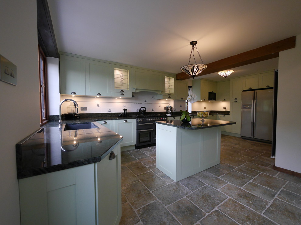 Photo of a large farmhouse u-shaped enclosed kitchen in London with a submerged sink, shaker cabinets, green cabinets, granite worktops, white splashback, ceramic splashback, black appliances, limestone flooring, an island, brown floors and green worktops.