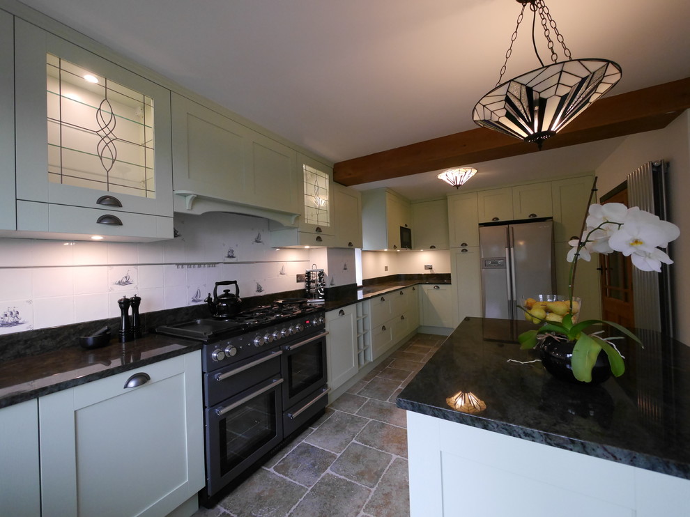 This is an example of a large rural u-shaped enclosed kitchen in London with a submerged sink, shaker cabinets, green cabinets, granite worktops, white splashback, ceramic splashback, black appliances, limestone flooring, an island, brown floors and green worktops.