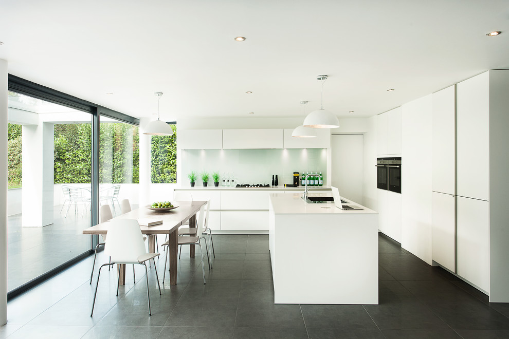 Идея дизайна: угловая кухня в современном стиле с обеденным столом, плоскими фасадами, белыми фасадами и фартуком из стекла