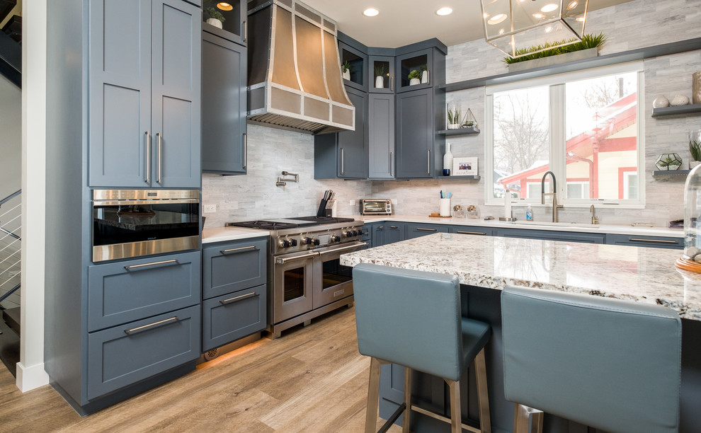 Large classic l-shaped kitchen/diner in Other with a submerged sink, flat-panel cabinets, engineered stone countertops, stainless steel appliances, an island, blue cabinets, grey splashback, medium hardwood flooring, brown floors and white worktops.