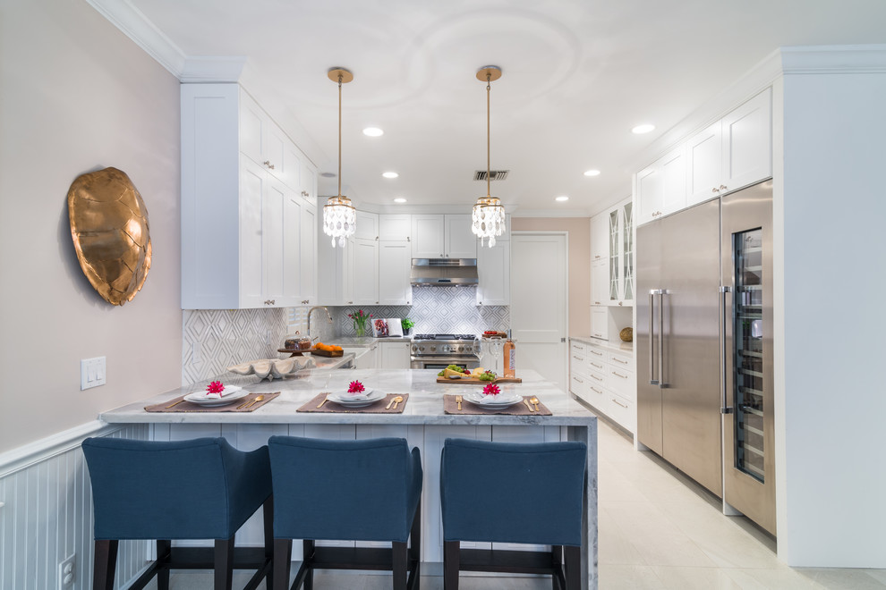 This is an example of a classic u-shaped kitchen in Miami with a belfast sink, shaker cabinets, white cabinets, stainless steel appliances, a breakfast bar and white floors.
