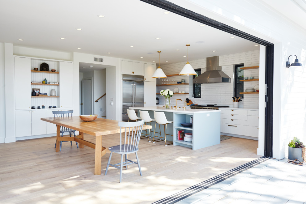 Foto de cocina lineal, contemporánea, grande, abierta, con fregadero sobremueble, armarios con paneles lisos, puertas de armario azules, encimera de cuarzo compacto, salpicadero blanco, salpicadero de azulejos de porcelana, electrodomésticos de acero inoxidable, suelo de madera clara, una isla, suelo beige y encimeras blancas