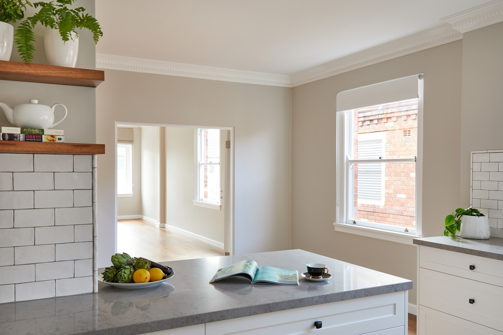 Example of a mid-sized classic u-shaped medium tone wood floor eat-in kitchen design in Sydney with shaker cabinets, white cabinets, subway tile backsplash, an island and gray countertops