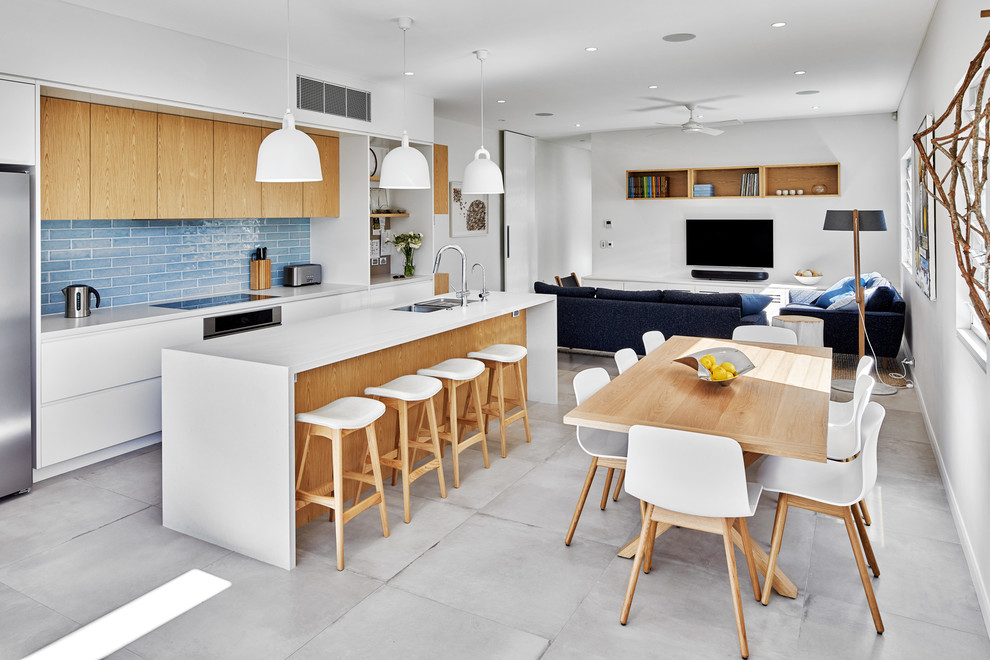 Foto på ett funkis vit kök, med en undermonterad diskho, släta luckor, vita skåp, blått stänkskydd, rostfria vitvaror, en köksö och grått golv