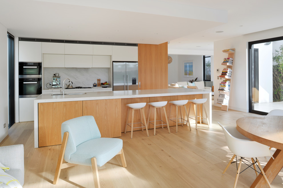 This is an example of a medium sized modern galley kitchen/diner in Sydney with light wood cabinets, composite countertops, stone slab splashback, stainless steel appliances, light hardwood flooring and an island.