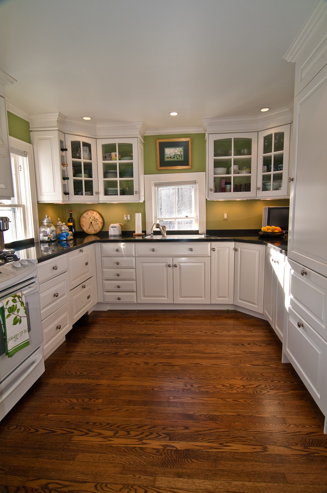 Example of a mid-sized classic galley dark wood floor enclosed kitchen design in New York with an undermount sink, raised-panel cabinets, white cabinets, stainless steel countertops, metallic backsplash, white appliances and no island