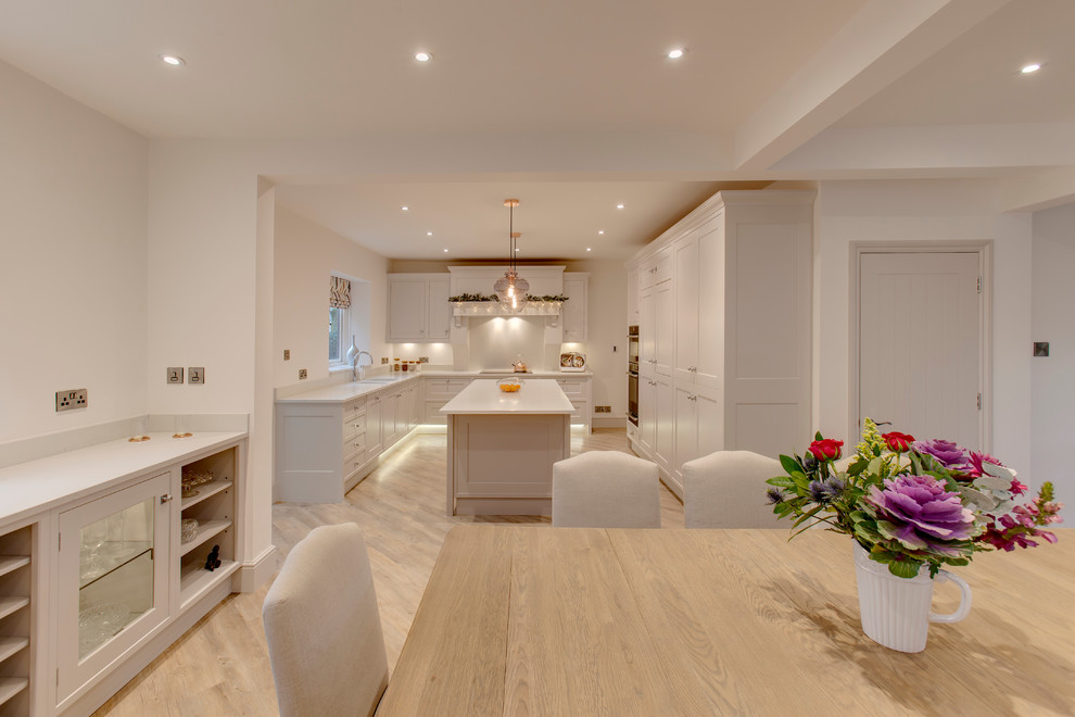 This is an example of a large traditional u-shaped open plan kitchen in Other with a double-bowl sink, beaded cabinets, white cabinets, quartz worktops, white splashback, stainless steel appliances, light hardwood flooring and an island.