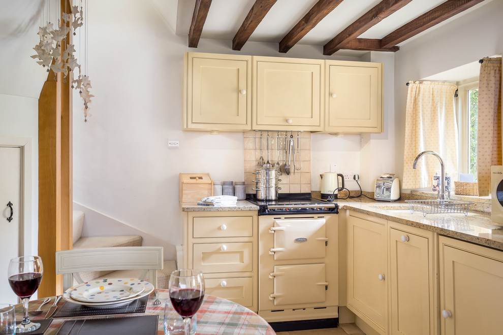 Eat-in kitchen - farmhouse l-shaped eat-in kitchen idea in Gloucestershire with an undermount sink, yellow cabinets, granite countertops, beige backsplash, porcelain backsplash, colored appliances, no island and beaded inset cabinets