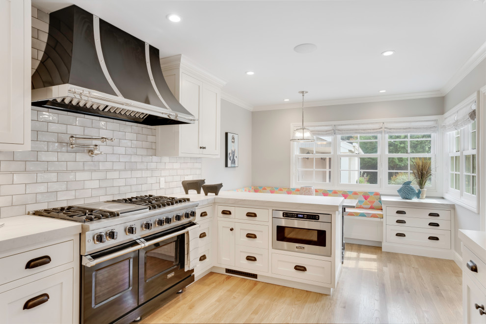 Transitional u-shaped light wood floor and beige floor eat-in kitchen photo in San Francisco with shaker cabinets, white cabinets, white backsplash, subway tile backsplash, black appliances, a peninsula and white countertops