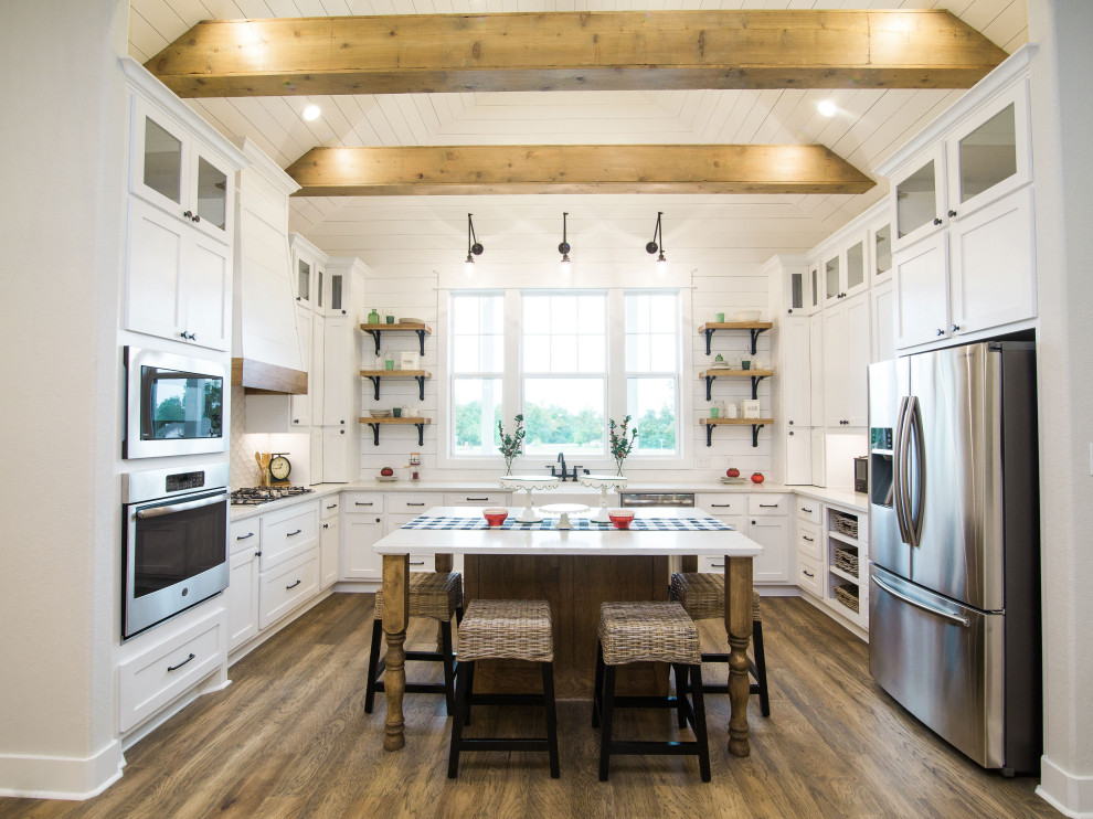 Inspiration for a farmhouse u-shaped kitchen in Austin with a belfast sink, shaker cabinets, white cabinets, stainless steel appliances, dark hardwood flooring, an island, brown floors, white worktops, exposed beams, a timber clad ceiling and a vaulted ceiling.