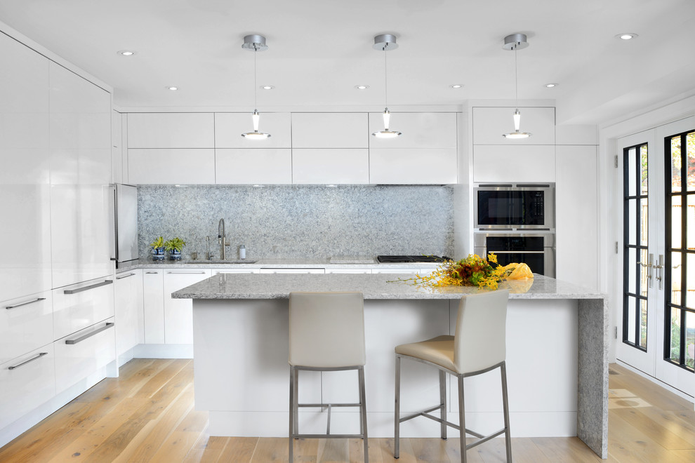 Photo of a contemporary l-shaped kitchen in Toronto with a submerged sink, flat-panel cabinets, white cabinets, grey splashback, stainless steel appliances, light hardwood flooring, an island and beige floors.