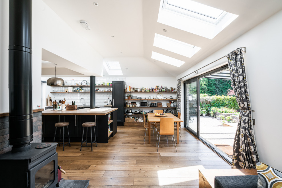 Inspiration for a contemporary galley open plan kitchen in Glasgow with black cabinets, white splashback, metro tiled splashback, medium hardwood flooring, an island, brown floors and a vaulted ceiling.